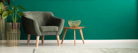 Close-up of a cozy, dark armchair and a wooden coffee table in a luxurious, green living room interior with golden decorationsの写真素材