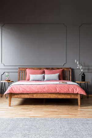 A large bed standing in a dark bedroom interior between bedside tables and in front of a grey rugの写真素材