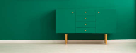Panorama of a minimalist, green living room interior with a modern, teal sideboard with drawers and wooden legsの写真素材