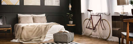 Elegant, dark bedroom interior with king-size bed and bike placed under the windowの写真素材
