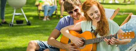Man teaching his girlfriend how to play guitar during grill partyの写真素材