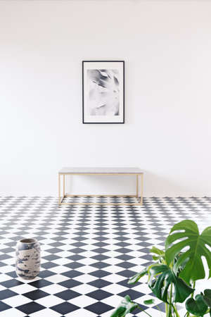 Spacious photography gallery in a minimalist black and white apartment interior with a golden frame, bench and a white, empty wallの写真素材