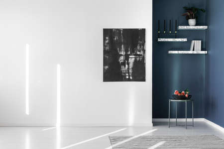 Black, abstract painting on an empty, white wall and marble shelves in a corner of a contemporary, minimalist apartment interiorの写真素材