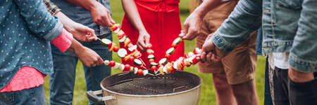 Panorama of friends standing in a circle grilling shashliks. Garden party meetingの写真素材
