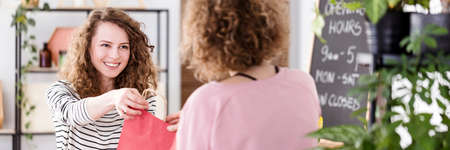 Smiling saleswoman giving natural cosmetics in pink bag to the buyer