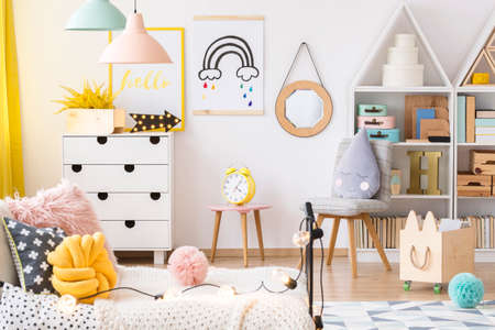 Bright children playroom interior with white cupboard, simple posters and raindrop pillow on chairの写真素材