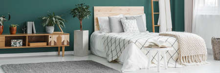 Double bed with wooden bedhead standing in green room interior with fresh plants and grey carpetの写真素材