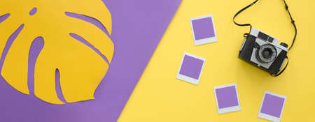Retro camera and mockup photos lying on a purple and yellow workspace area with monstera leafの写真素材