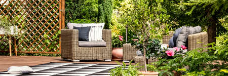 Garden armchair with pillows standing on wooden terrace with black and white carpet