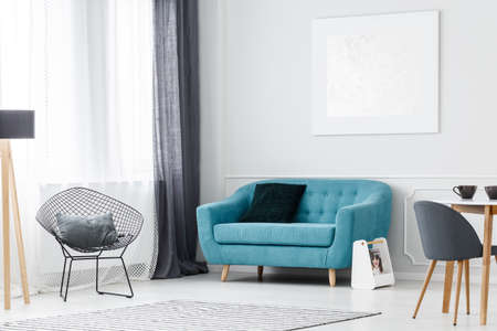 Modern, silver painting hanging above turquoise couch with pillow standing next to diamond chair in elegant flat interior for rentalの写真素材