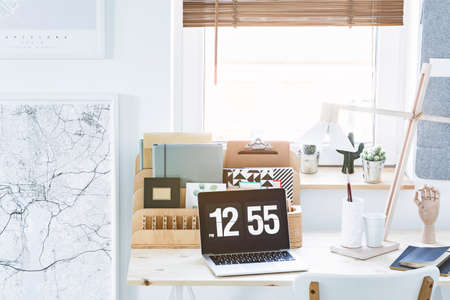 White and black map, wooden desk organizer and laptop with a clock set on a desk by the windowの写真素材