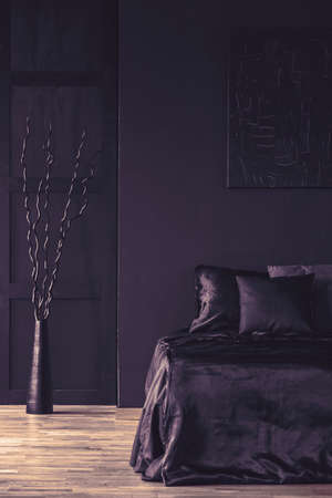 Metal sculpture next to bed with black bedding in monotone bedroom interiorの写真素材