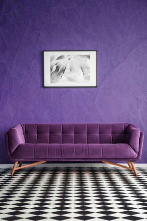 Poster on violet wall above suede sofa in living room interior with checkerboard floor