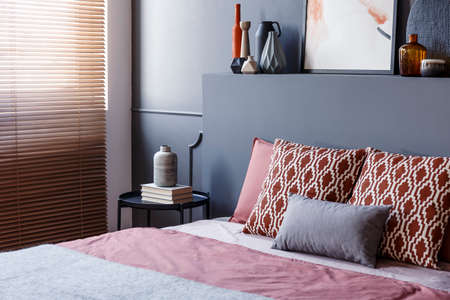 Close-up of patterned pillows lying on a soft bed in bedroom interior with black walls, decorative...