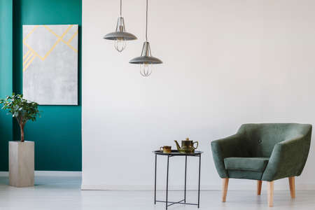 Modern, green and white room with teapot set on the table, armchair, plant in a pot, marble on the wall and lampsの写真素材
