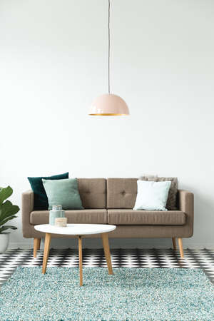 Pastel lamp above white round table near brown sofa in simple living room interiorの写真素材