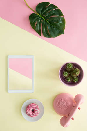 Top view of a duotone table with a green leaf, cactus, tablet, doughnut and retro phoneの写真素材