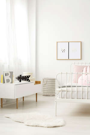 Black arrow led light on a scandinavian style sideboard and a checked laundry basket in a white child's bedroom interiorの写真素材