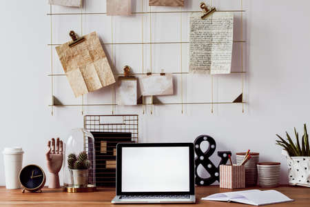 Laptop, cactus, decorations and notebook on a wooden desk and a metal wall organizer above itの写真素材