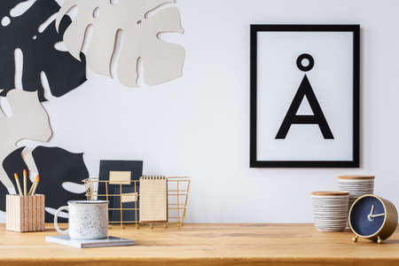 Wooden desk with clock, mug, pencils and paper leaf wall decoration next to a poster