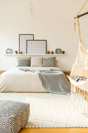 Patterned cushions on bed against white wall with posters on shelf in scandi bedroom interior