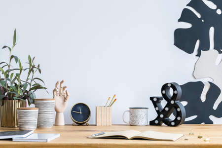 Messy desk with a plant in a golden pot, wooden hand, clock and leaves on the wallの写真素材