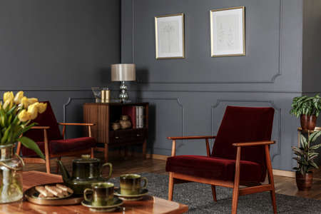 Posters on grey wall with molding in living room interior with red wooden armchairの写真素材