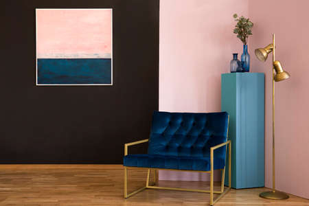 Navy blue armchair next to a gold lamp in black and pink living room interior with paintingの写真素材