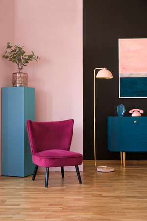 Red velvet armchair in pastel living room interior with pink lamp next to a navy blue cabinetの写真素材