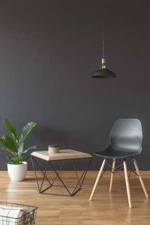 Plant, simple chair and wooden coffee table set on black, empty wall in living room interiorの写真素材