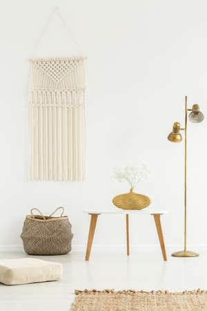 Beige DIY macrame on a white wall, wooden furniture and golden decorations in a boho living room...