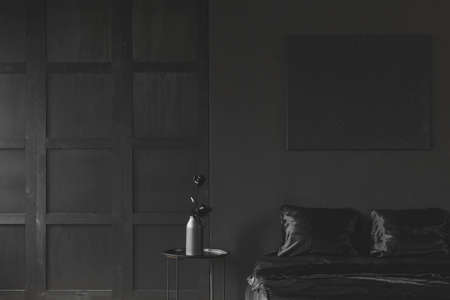 Rose on the table next to bed in monotone dark black bedroom interior with wooden molding on the wallの写真素材