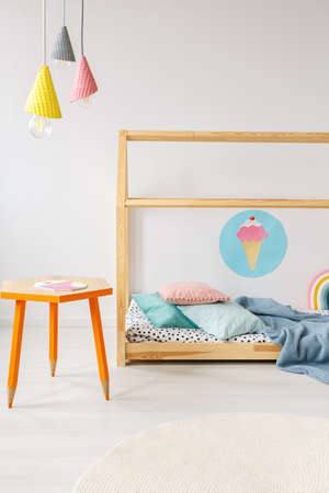 Orange table under colorful lamps in modern child's bedroom interior with wooden bedの写真素材