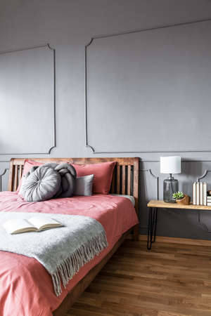Book on blanket on wooden pink bed against grey wall with molding in cozy bedroom interiorの写真素材