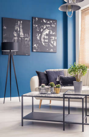 Black industrial coffee table with marble top in a stylish living room interior with black art on...