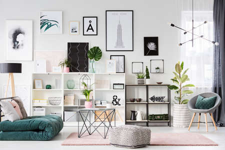 Patterned pouf and table on pink carpet next to green futon in pastel living room interior with galleryの写真素材