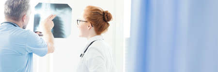 Header with an orthopedist consulting a broken bone with his female colleague, pointing to a...