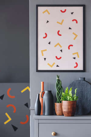 Patterned poster on grey wall above cabinet with vase and plants in living room interiorの写真素材