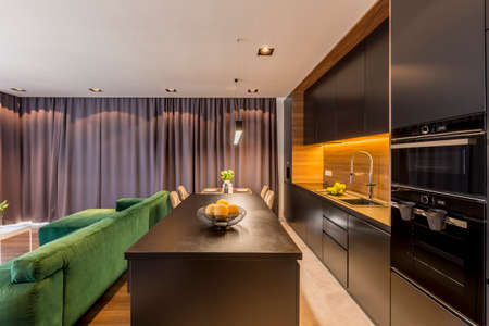 Kitchen island in dark open space interior with green couch and brown drapesの写真素材