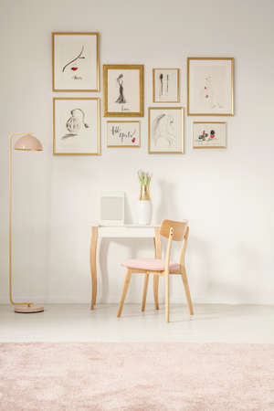 Wooden pink chair at dressing table next to gold lamp in feminine flat interior with gallery of...