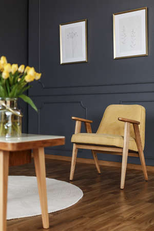 Yellow wooden armchair under posters in grey living room interior with tulipsの写真素材