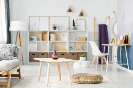 Close-up of vase on wooden table next to a pouf and beige settee in living room interior