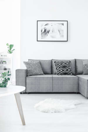 Comfortable corner sofa with patterned pillows, fur rug and delicate painting on the white wallの写真素材