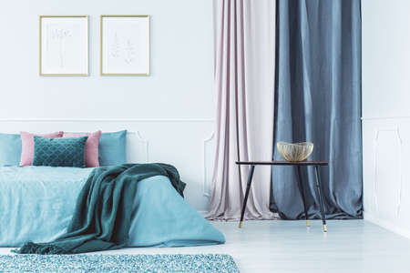Two simple posters in gold frames hanging on the wall above double bed standing in bright interior...