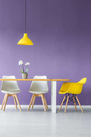White floor and purple wall living room interior with simple, contrasting color chairs, table with a...