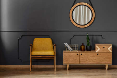 Simple black room interior with wooden floor, yellow chair, mirror and cabinet