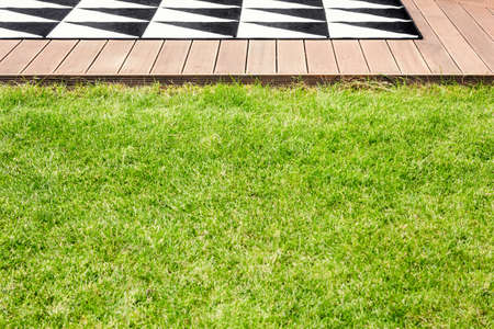 Green grass and a wooden terrace with geometrical rug in a garden