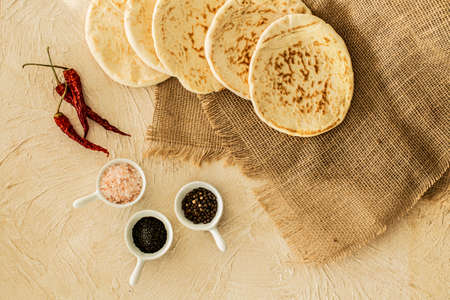 Top view of pita bread on burlap fabric, red chili peppers and cups with spices on a beige surfaceの写真素材
