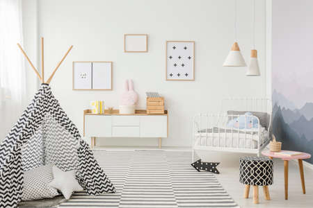 Patterned tent near stool in child's bedroom interior with posters on white wall above wooden cupboardの写真素材