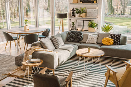 High angle view of a stylish, nordic living room interior with a wooden dining table, gray sofa and view on terrace and backyard. Real photoの写真素材
